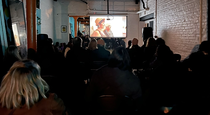 Host a Screening Prodigal Daughter screening the film 2 Audience seated in a dimly lit room watching Prodigal Daughter projected on a screen during an indoor community screening.